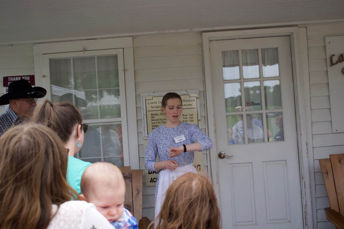 A woman speaks to a small group outside a building, checking her watch near a glass door.