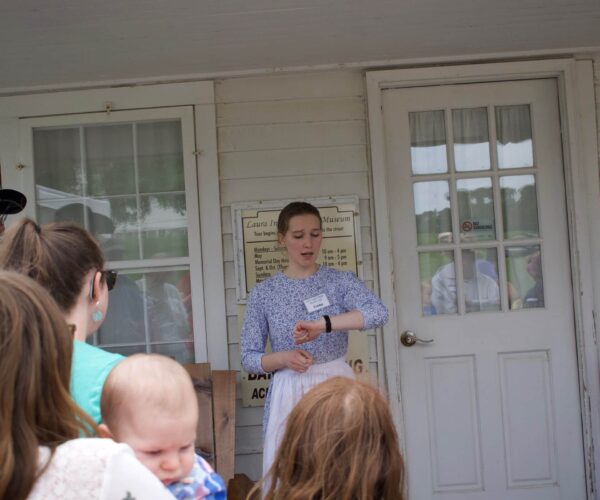 A woman speaks to a small group outside a building, checking her watch near a glass door.