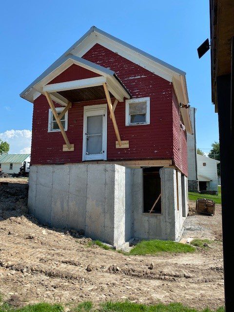 A small red house sits elevated on a new concrete foundation at a construction site.