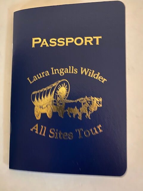Blue "Passport" booklet featuring a gold wagon and oxen graphic, labeled "Laura Ingalls Wilder All Sites Tour.