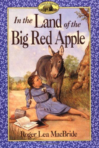 A girl in a blue dress sits on grass beside a donkey, with an open book titled "In the Land of the Big Red Apple" nearby; book title appears above.