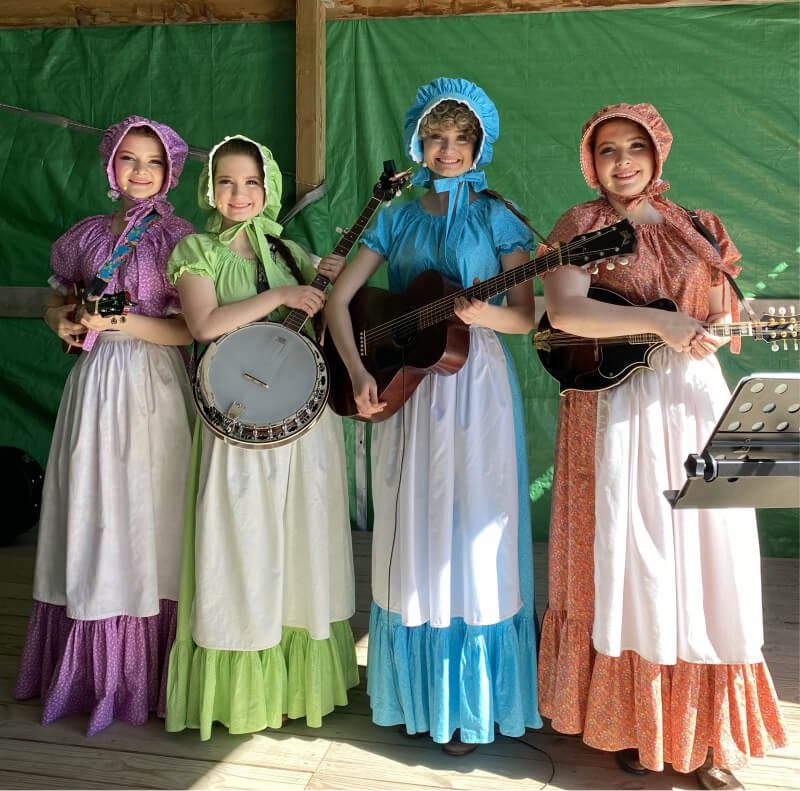 Four women dressed in period clothing each holding various instruments