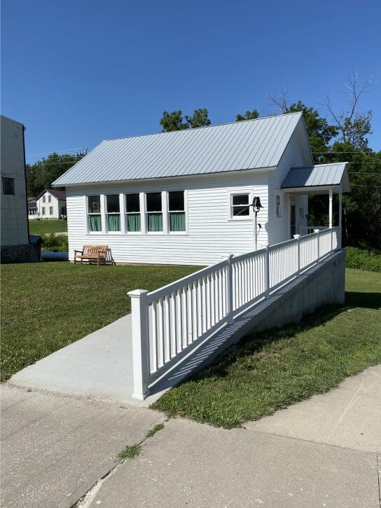 Small white building with ramp, green lawn, and clear blue sky in the background.