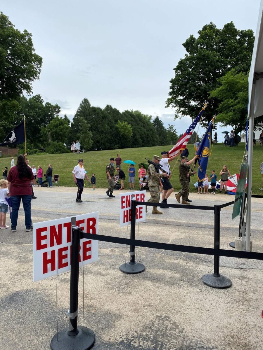 A color guard marches in a parade as people watch from the roadside, with 