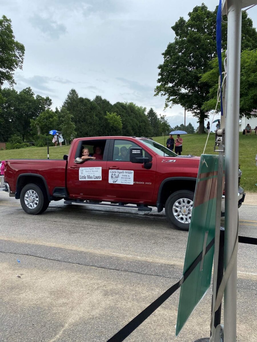 A red pickup truck in a parade with a sign reading 