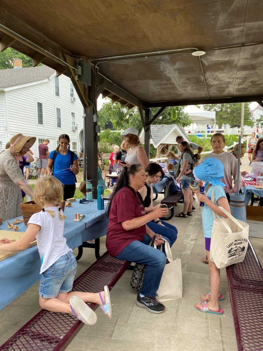 People gather under a pavilion at a community event, with children and adults enjoying food and conversation.