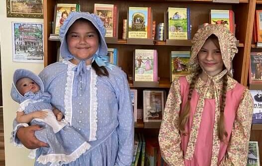 2025 Little Miss Laura contestants stand in front of a bookshelf; one holds a matching doll.