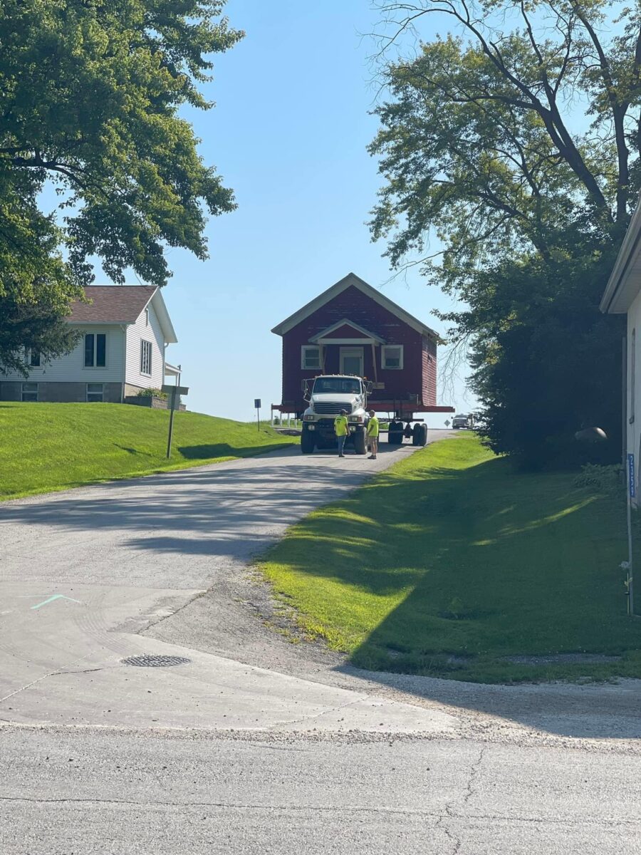A house is being transported on a truck up a residential street on a sunny day.