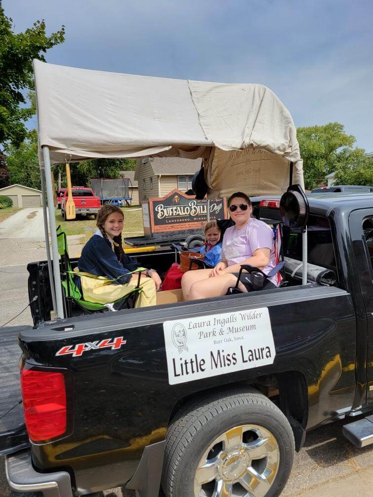 Three girls sit in a covered truck bed labeled 